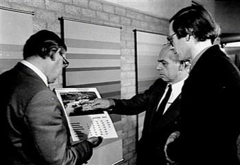 van Rijn, directeur A-Faculteiten (midden), bekijkt de nieuwe kalender (1980) met 12 luchtfoto's van het landgoed Heyendael en de KU van 1910 tot 1979, samen met de fotograaf Spaan (links); Foto Foto