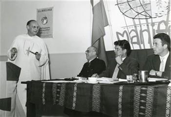 De witte pater Mgr. Blomjous, missiebisschop in Tanzania spreekt op een bijeenkomst van de KAJ-wereldwijd, terwijl A.H. Huijboom, Gerard van Brakel en Huub Larosch luisteren; Foto Foto