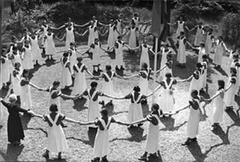 Leerlingen van Huize Driekoningen dansen in een kring. Bevat het bijschrift: "Heb je al gehoord van de zeven, de zeven"; Foto Foto