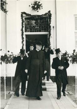 Op de dag van de viering van zijn 40-jarig priesterfeest verlaat pastoor van Welie de pastorie en wordt daar begeleid door het kerkbestuur. Bijschrift: "Het kerkbestuur wapent zich voor de strijd"; Foto Foto