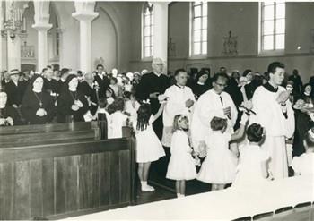 Op de dag van de viering van zijn 40-jarig priesterfeest betreedt pastoor van Welie omringd door als bruidjes verklede meisjes de kerk. Bijschrift: "Vol dankbaarheid op naar het altaar"; Foto Foto