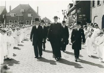 Op de dag van de viering van zijn 40-jarig priesterfeest loopt pastoor van Welie samen met het kerkbestuur, omringd door bruidjes naar de kerk. Bijschrift: "Triomfantelijke tocht, temidden van zijn naaste medewerkers "; Foto Foto
