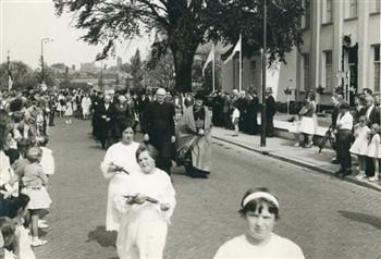 Defilé bij de viering van het 40-jarig priesterfeest van pastoor van Welie. De pastoor sluit zich aan bij de optocht nadat deze pastorij is gepasseerd. Bijschrift: "Nog was het niet genoeg......."; Foto Foto
