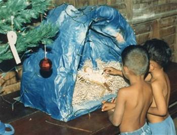 Kinderen die verzorgd worden door de Soon Klang Thewa Association te Bangkok bij een kerststal. Bijschrift: "Christmas seasons are also organised for the children to recall the spirit and the good deeds of those founders and sponsors and to realise the importance of the seasons and to receive the holy blessings and happiness"; Foto Foto