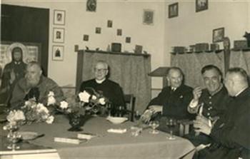 Het apostolaat der Hereniging heeft kardinaal Tisserant uitgenodigd. De kardinaal (helemaal links) zit aan tafel met de voorzitter van het Apostolaat, pastoor A.G. Smit (met bril). De man in uniform is W. Croon, toegevoegd gentilhomme. De foto's 6a1455, 6a1456, 6a1457 en 6a1458 hebben allemaal betrekking op het bezoek van deze kardinaal aan Nederland; Foto Foto