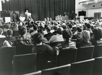 Spreekster en publiek in de zaal, met tekst 'lustrum KUN 1923-1988'; Foto Foto