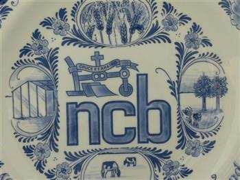 Wandbord, met embleem van de Noord-Brabantse Christelijke Boerenbond en tekst 'Noordbrabantse Christelijke Boerenbond', houdende afbeeldingen van bloemen, koeien, een varken, kippen, een kas, bomen en graan. Op achterzijde tekst 'Pastoor H. van de Wijngaard Geestelijk adviseur Boerenbond Mariaheide 1976-1995' en 'Delft Plateelbakkerij Schoonhoven Holland'; Wandbord Wandbord