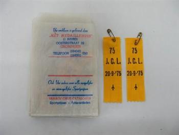 Veertien leiders-insignes in twaalf papieren zakjes. Met tekst: '75 J.C.L.; Insigne Insigne